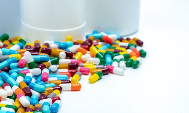Colorful capsule pills near plastic drug bottle. Multi-colored capsule pills on white table. Pharmacy drugstore products. Pharmaceutical industry. Health budget and policy. Bright color capsule pills.