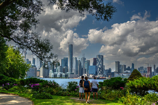 Toronto city skyline framed by trees and garden foliage viewed from Wards Island on a sunny August day with dramatic clouds
