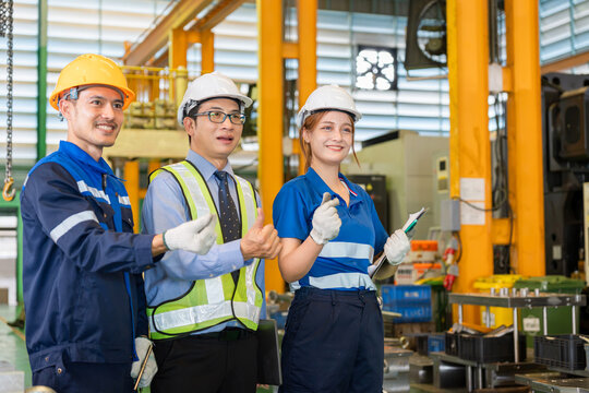 Manufacturing workers and supervisor making finger heart sign in plant, Diverse team of industrial engineers and workers smiling in factory, Industrial team posing together inside factory