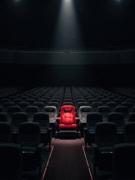Single Red Seat Illuminated in a Dark Empty Movie Theater Auditorium with Spotlight.