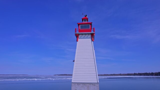 Epic view of lighthouse beacon surrounded by early April melting spring ice formation with calm glass like lake water. Sunny warm and cozy spring day with blue sky horizon over water.