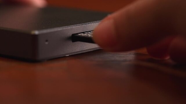 Macro shot of human hand inserting CFexpress Type A card into professional aluminum reader with green LED light on wooden desk, digital media data transfer and photography workflow concept.
