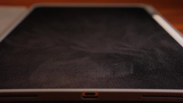 Close up shot of spraying liquid cleaner on tablet screen and wiping vertically up and down with soft microfiber cloth, surface disinfectant and screen care concept.