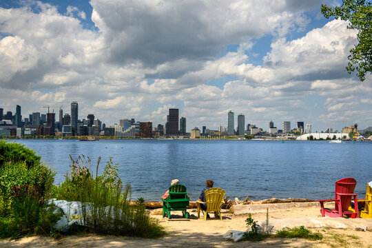 Colorful Adirondack chairs on a Wards Island beach with people relaxing and viewing the Toronto skyline on a summer day