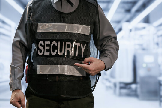 Close-up of a security guard in uniform wearing a protective vest and pointing at a security badge in a modern indoor building.
