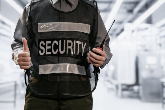 Close view of a security guard in a protective vest holding a radio and giving a thumbs up in a bright modern building.