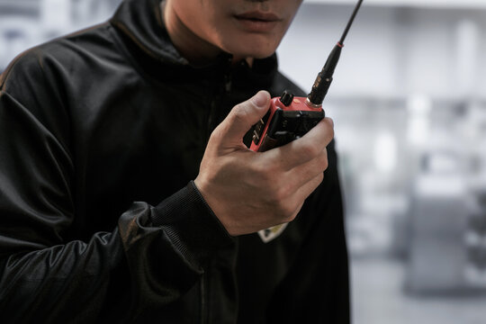Close-up of a security worker in black jacket using a handheld radio indoors, with a blurred modern office background.