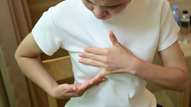 Young Asian woman touching her breast for checking breast size or cancer awareness. Breast self-exam alone is not sufficient to detect breast cancer early.