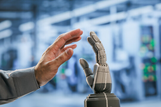 Close view of a human hand reaching toward a robotic hand in a bright modern factory, connection between people and automation.