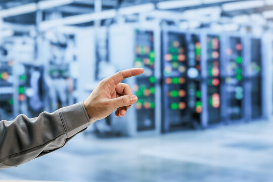 Close-up of a technician's hand pointing at blurred server racks with glowing status lights in a modern data center.