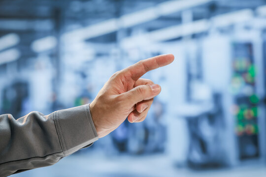 Close-up of a worker's hand pointing at blurred industrial equipment in a modern factory, control, inspection, guidance and automation.