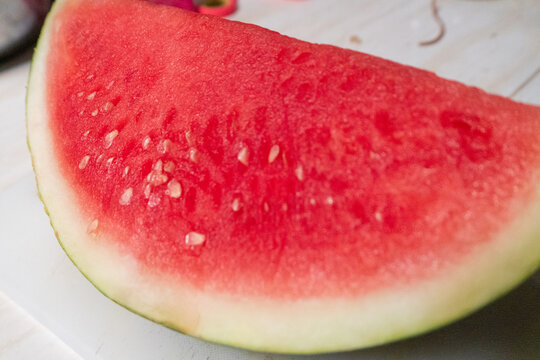The watermelon is fresh and bright red, featuring clearly visible black seeds and a green rind. It has juicy red flesh, a light green rind, and small seeds.