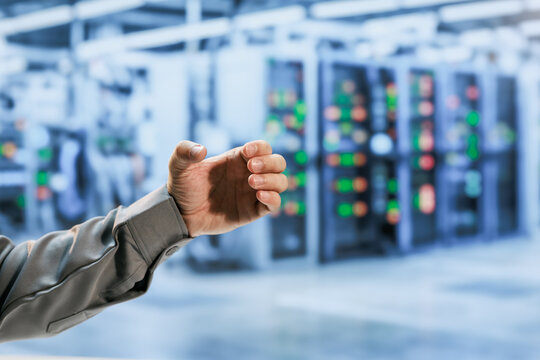 Technician hand gesturing in a modern data center with blurred server racks and colorful status lights, network monitoring and technology control.