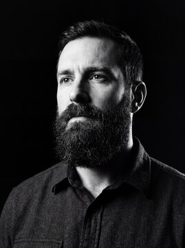 Introspective man with beard in chiaroscuro portrait emphasizing intense gaze.