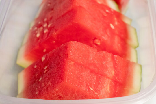 Bright fresh red watermelon, neatly cut into triangles and arranged in a container. Bite sized triangular pieces for snacking, kept refrigerated.