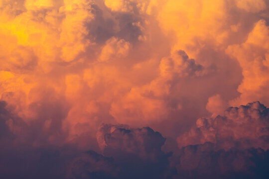Golden cumulonimbus storm clouds illuminated by warm sunset light, creating dramatic atmospheric textures and towering cloud formations for weather, climate and nature backgrounds.