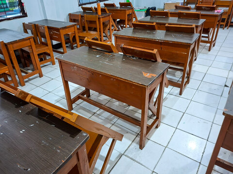 An indoor shot showing multiple rows of classic wooden desks and chairs neatly arranged inside a brightly lit, tiled classroom.