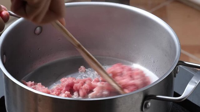 Close-up of cooking minced pork in boiling water and stirring with a wooden spatula in a pot, preparing ingredients for Thai cuisine