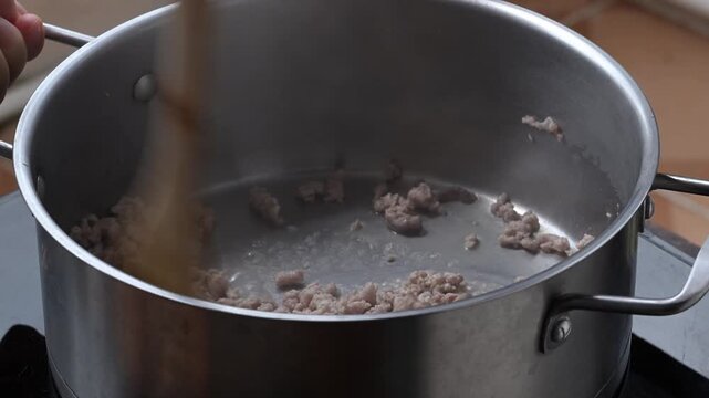 Close-up of cooking minced pork in boiling water and stirring with a wooden spatula in a pot, preparing ingredients for Thai cuisine