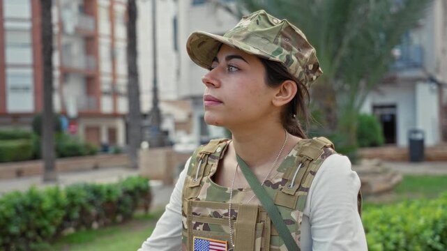 Woman soldier salutes with right hand wearing camouflage vest and visible us flag patch in street; pride duty.