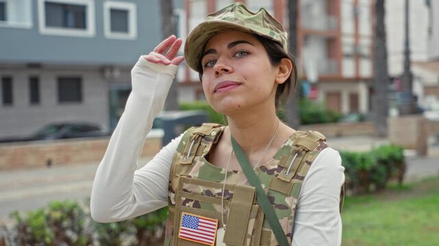 Young woman soldier tips cap with hand and displays us flag patch on vest in an urban street setting; pride duty.