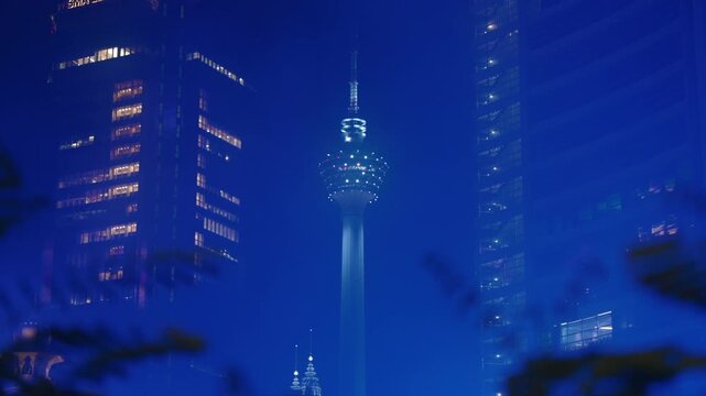 Close up of KL Tower Between Skyscrapers in Blue illuminated fog from River of Life at night