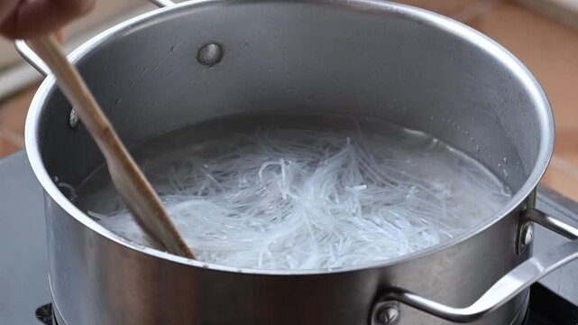 Close-up of blanching fresh glass noodles in a pot of boiling water, preparing ingredients for Thai spicy glass noodle salad (Yum Woon Sen)