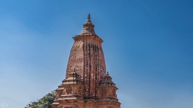 Ancient Newar architecture. A red brick Shiva temple in the shikhara  style. A tall domed tower, a spire on top. Clear blue sky. Nepal. Kathmandu. Jagharnath temple 