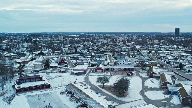 Aerial drone shot shows snow covered residential area with houses, streets, rooftops, trees, and open spaces across winter landscape during cold winter day in Vaxjo, Smaland, Sweden