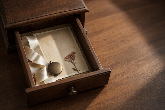 Open Wooden Drawer With A Vintage Locket Satin Ribbon And Pressed Flower Resting On A Blank Card