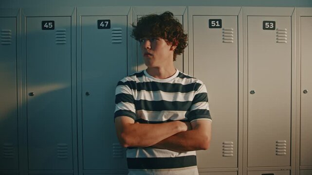 Close Up of Thoughtful High School Student Stands by Lockers and Follows Classmates With Eyes in Bright Corridor, Expressing Curiosity, Loneliness and Quiet Observation During School Break. Portrait.