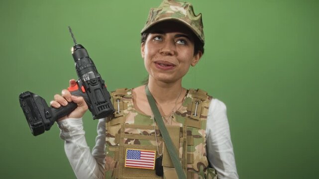 Woman soldier in army uniform holds cordless drill by handle, finger on trigger, american flag patch visible, photographed in studio; pride.