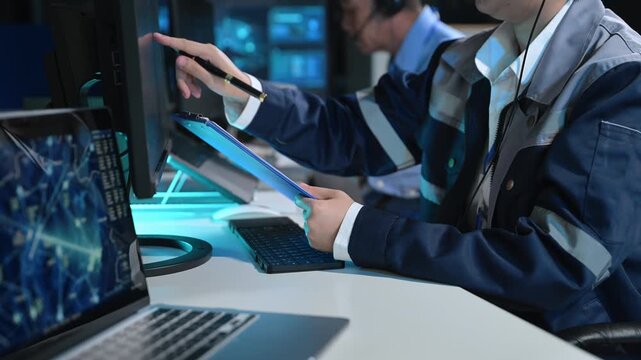Asian engineer in headset analyzes radar screens and takes notes in a high-tech control room, managing telemetry