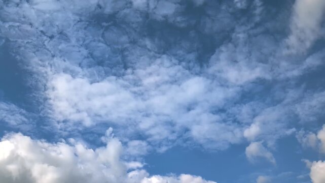 Camera panning right showing white cumulus clouds on a blue sky. Candid smooth movement shot of cloudscape background on a bright sunny day with natural lighting.