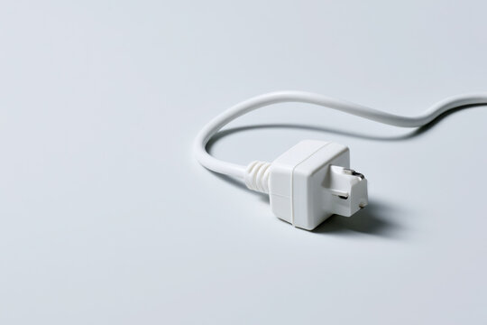 White electrical plug and power cord isolated on a pale background with generous copy space, representing electricity, connection, energy and household technology.