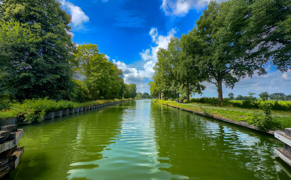 long canal leading toward distant horizon with guiding posts and vivid sky. strong linear composition, calm water lanes, framed