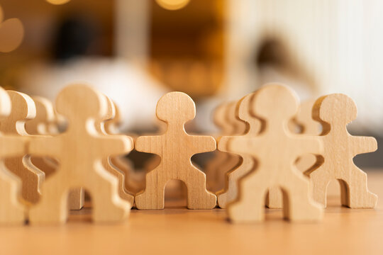 Human resources and teamwork concept with crowd of wooden people figures standing together on table with warm bokeh background for workforce management, community unity and recruitment.