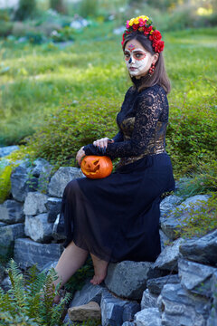 Halloween beauty portrait of woman with Halloween pumpkin in hand. Santa Muerte makeup.