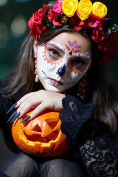 Halloween beauty portrait of woman in forest with Halloween pumpkin in hand. Santa Muerte makeup.