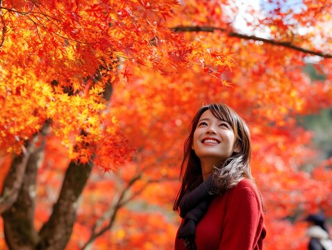 紅葉に染まる楓の下で見上げて微笑む女性の秋の散策観光イメージ写真