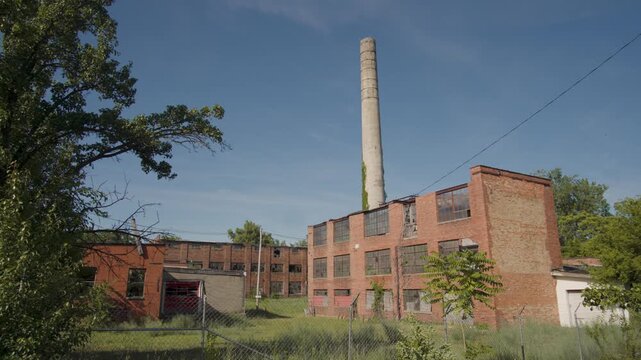 Extreme wide shot of an abandoned factory made of brick with a towering smokestack (tilt up)