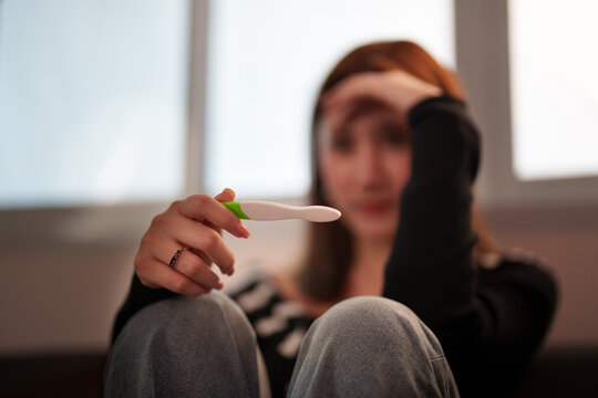 Stressed woman holding pregnancy test stick at home with anxious expression
