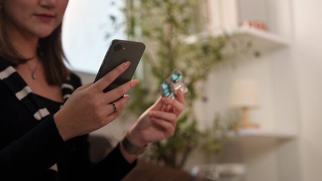 Woman holding smartphone and medicine blister pack at home for online pharmacy and telehealth
