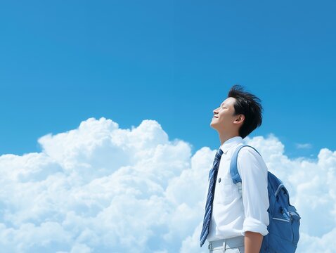青空と白い雲の下で未来を見上げながら深呼吸するリュック姿の男子学生の爽やかな一瞬