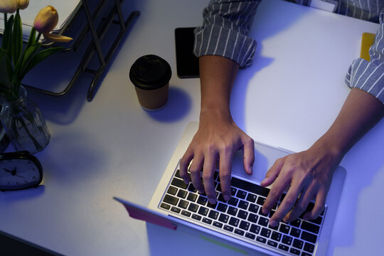 Top down view of hands typing on laptop working late at desk