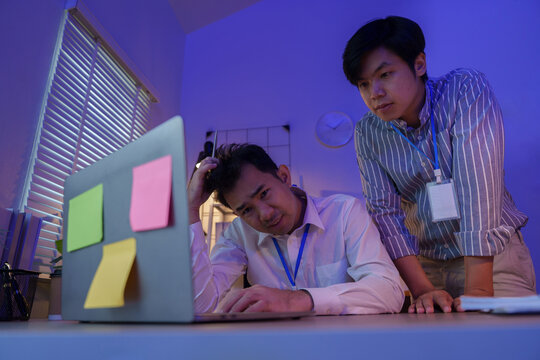 Asian businessmen collaborating and solving problems while working late on laptop