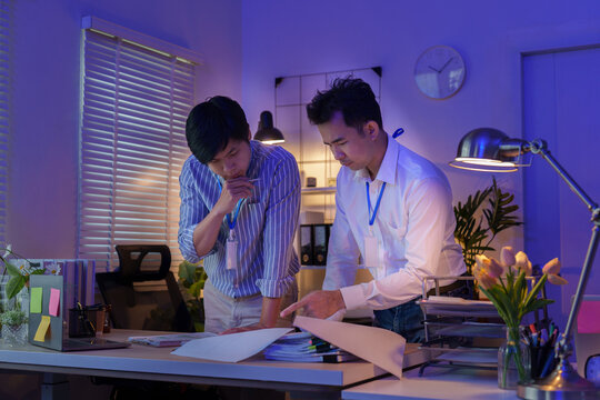 Two Asian businessmen collaborating on financial reports while working late in office