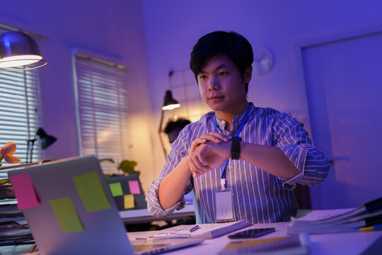 Asian businessman checking smartwatch while working late in night office