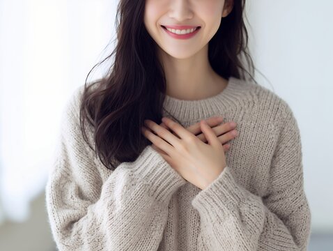 胸に手を当てて優しい笑顔を浮かべるセーター姿の女性が伝える感謝の気持ち