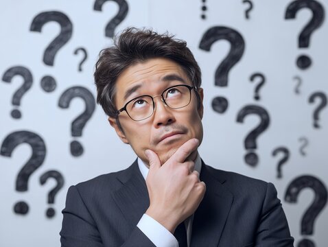 疑問符に囲まれて顎に手を当てながら考え込むスーツ姿のビジネスマンが意思決定に悩む場面